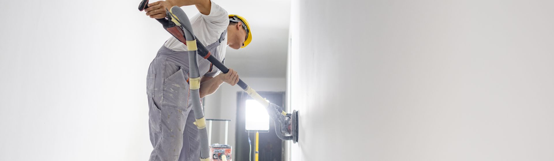 Männliche Person schleift mit einer sogenannten "Giraffe" die Wandoberfläche glatt