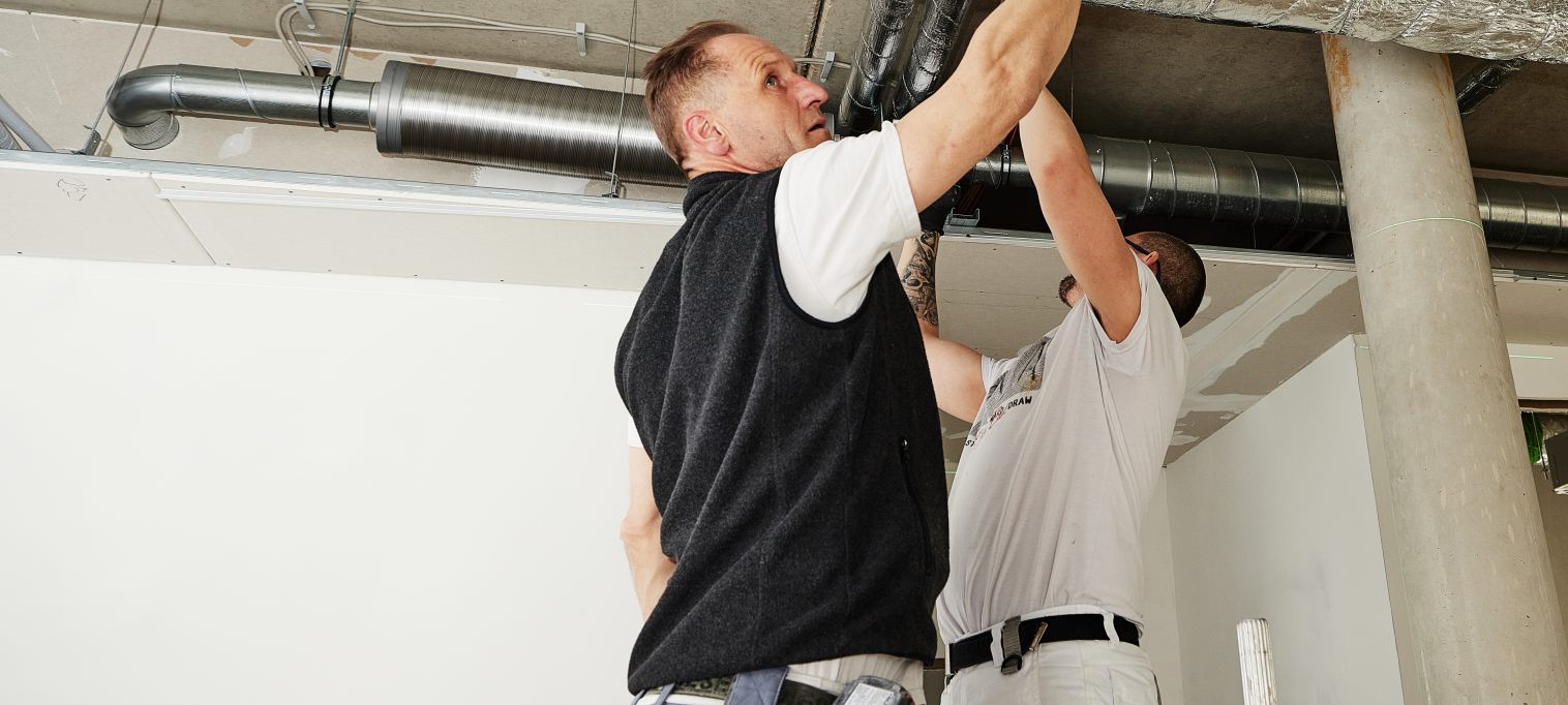 Zwei Maler auf einer Baustelle, arbeiten an der Decke und hängen diese ab.
