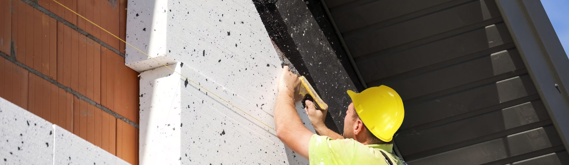 Mann auf einem Gerüst steht an der Giebelseite eines Hauses und verkleidet es mit Dämm-Elementen