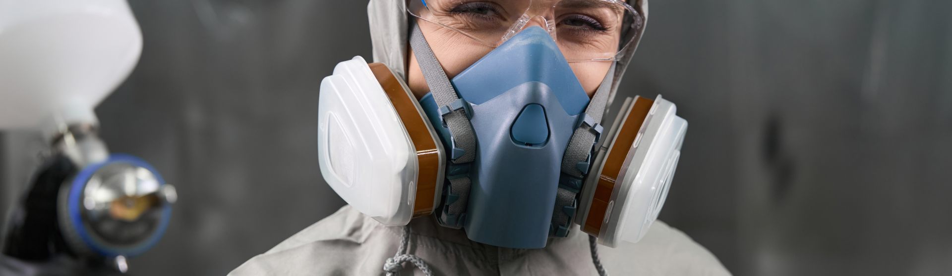 Auszubildnende in Schutzanzug, Schutzmaske und Spritzpistole lächelt in die Kamera