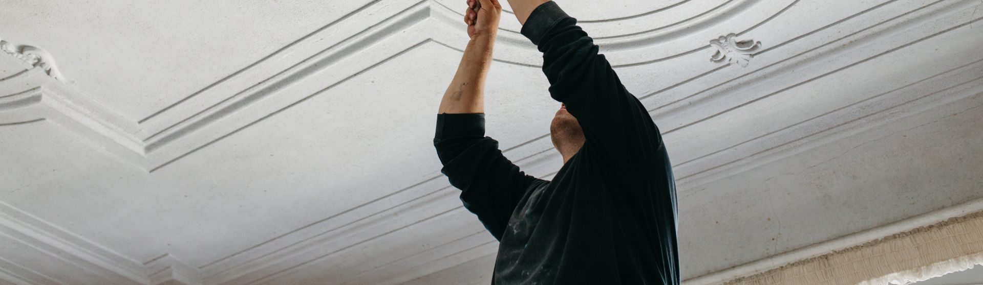 Mann auf mobilem Gerüst arbeitet an ornamentalen Stuckelementen einer Zimmerdecke