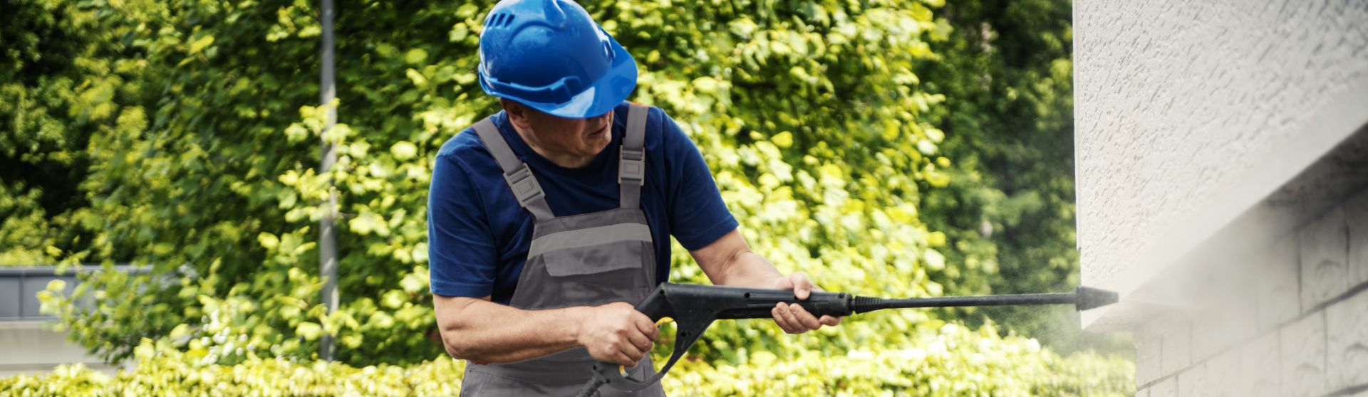 Mann mit Dampfstrahlerlanze in der Hand reinigt den Sockel eines Hauses 