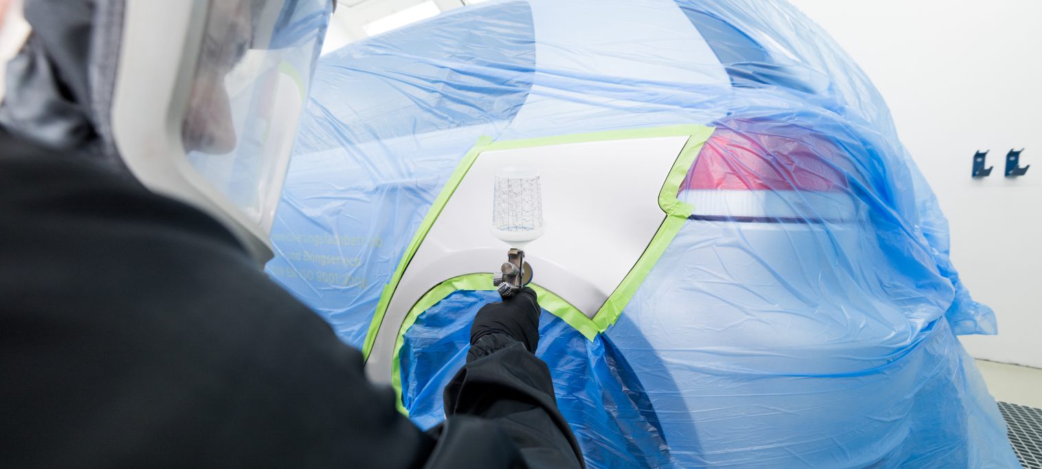 Lackierer in voller Ausrüstung in der Seitenansicht beim Lackieren eines Fahrzeuges